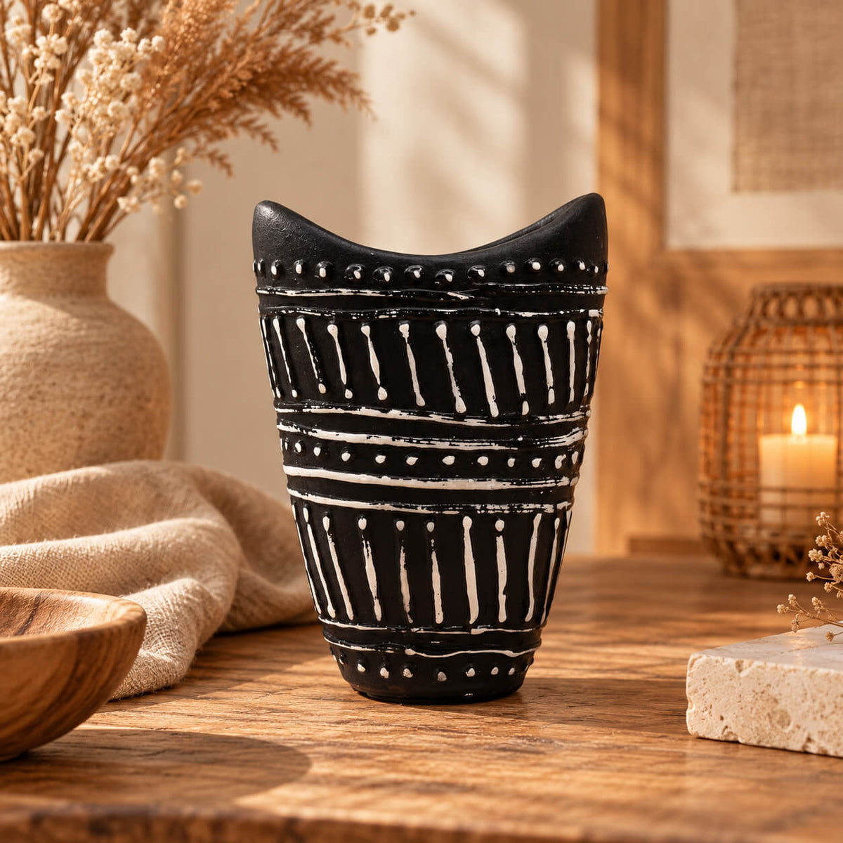 Vase en terre cuite brun chocolat à motifs blancs en relief, ouverture ovale à deux pointes, posé sur une table en bois